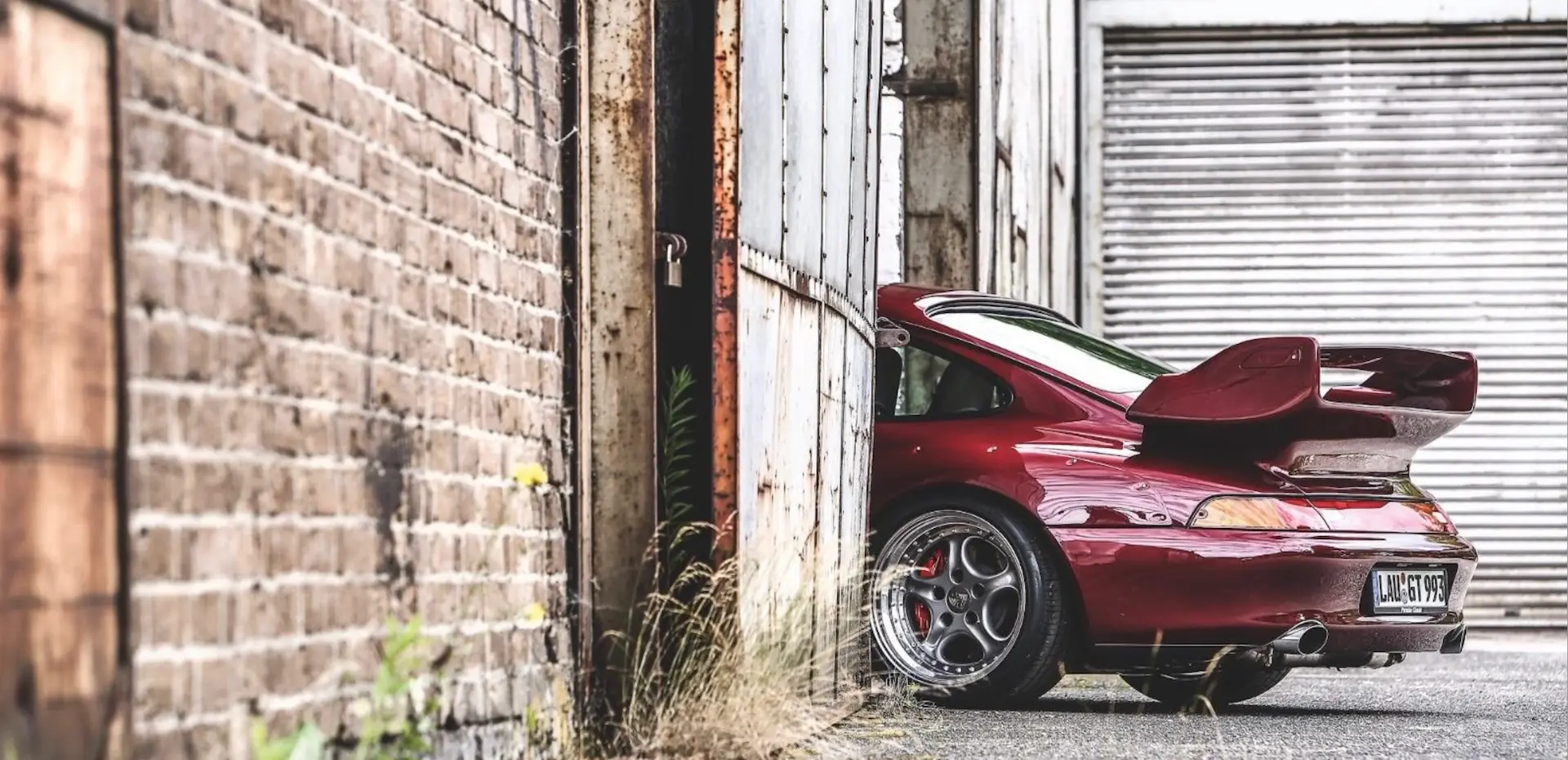 Red Porsche 911 GT2 peeking from behind an industrial warehouse wall