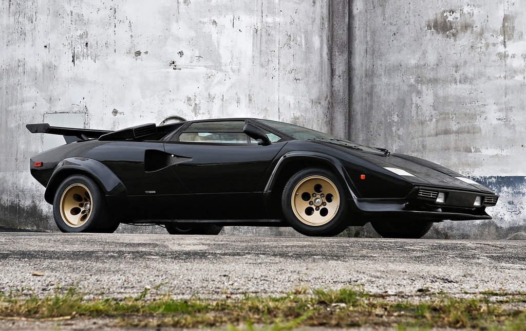 Black Lamborghini Countach with gold wheels parked against a concrete wall